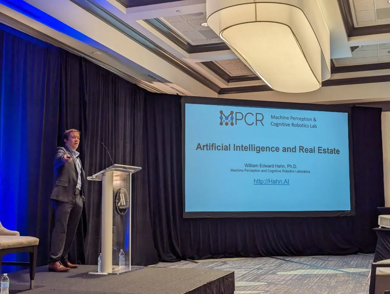 Dr. William Hahn presenting at the AI and Real Estate conference, with his Machine Perception and Cognitive Robotics Lab title slide on screen